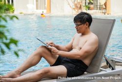 Man reading on digital reader by poolside 4ZDm90
