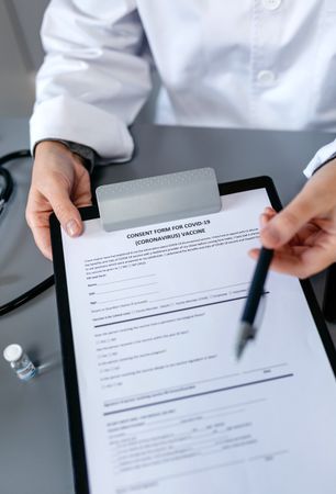 Unrecognizable doctor offering pen to sign coronavirus vaccine consent form