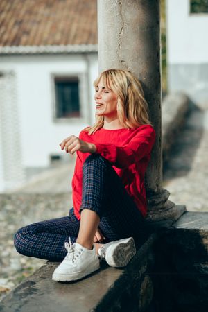 Happy blond woman sitting on cement stoop with pillar in Spanish town