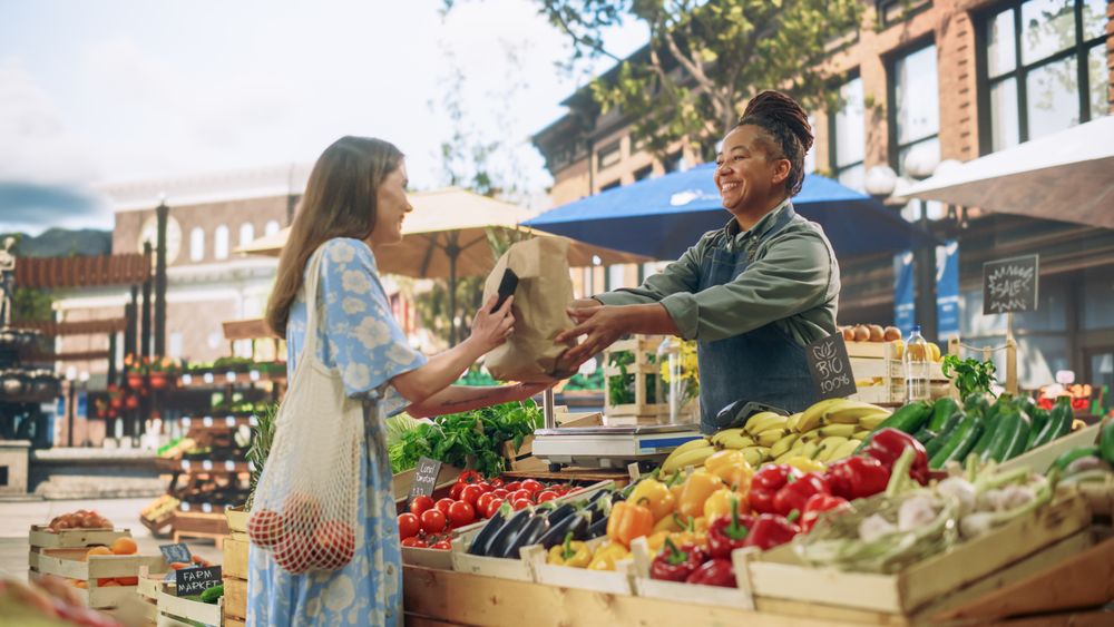 Female Customer Buying Sustainable Organic Vegetables From a Joyful Black Female Farmer on a Sunny Summer Day.