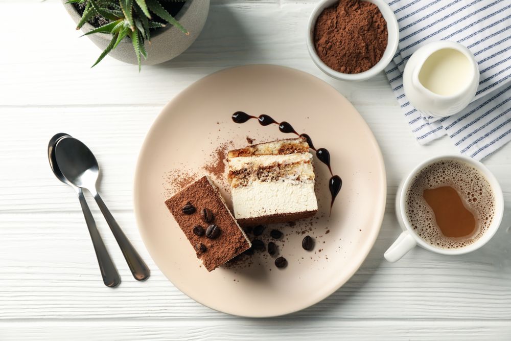 Composition with tasty tiramisu and cocoa drink on light wooden table. Delicious dessert