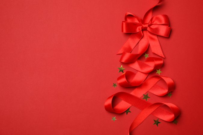 Red ribbon and glitter stars on red background, space for text