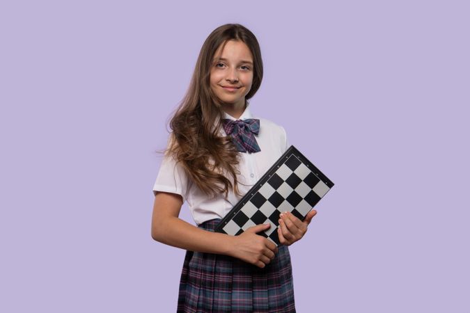 Girl in white shirt and plaid skirt holding checkerboard