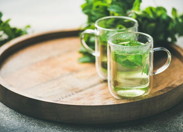 Side view of mint tea with fresh mint leaves on wooden tray, with copy space
