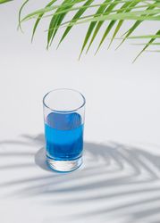 Cold blue drink in glass under green palm branch
