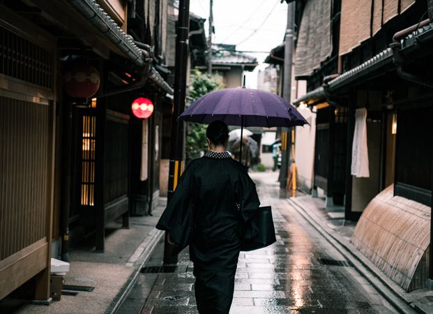 Back view of woman wearing kimono holding an umbrella walking in an alley
