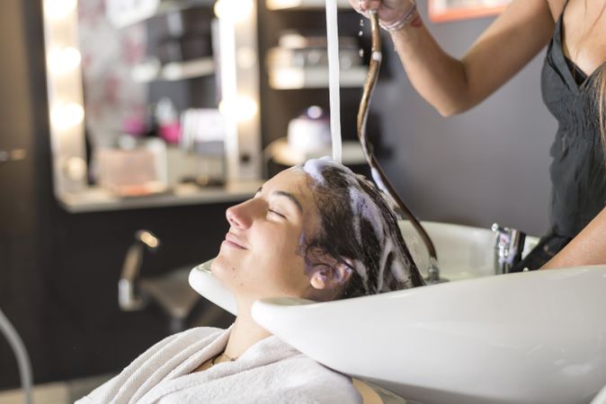 Smiling female having her hair washed by stylist