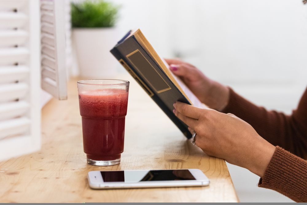 Anonymous Black woman drinking smoothie and reading book in bar