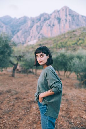 Woman with hand in pocket in beautiful park with hills and olive trees
