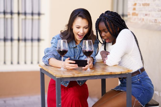 Female friends at a restaurant with red wine looking at phone