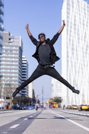 Black man wearing casual clothes jumping against city background