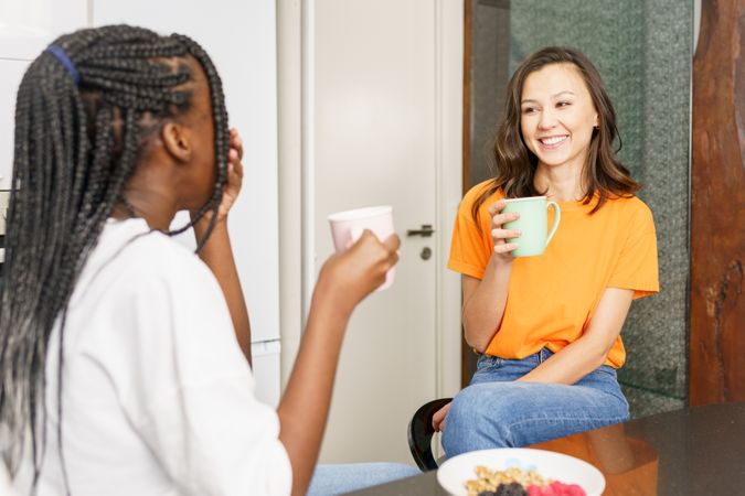 Two women chatting and smiling over coffee in the kitchen