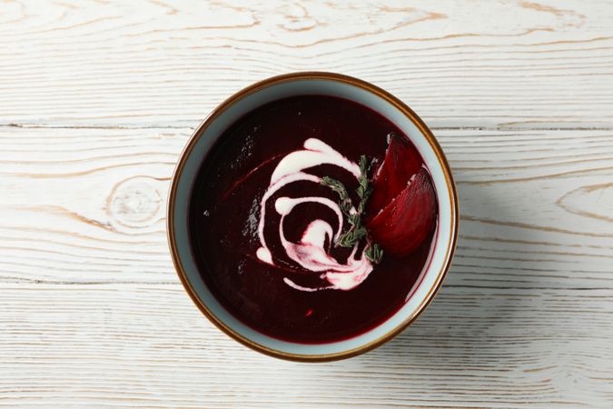 Looking down at bowl of borscht or beetroot soup on wooden table