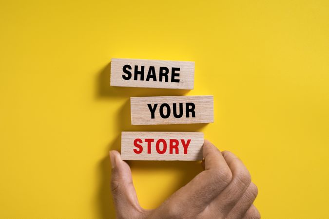 male hand put put share your story words on wooden blocks isolated on yellow background