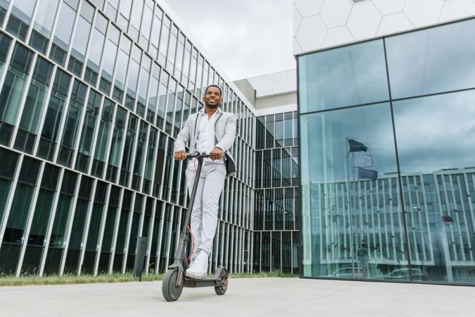 Black man in suit on electric scooter in business center