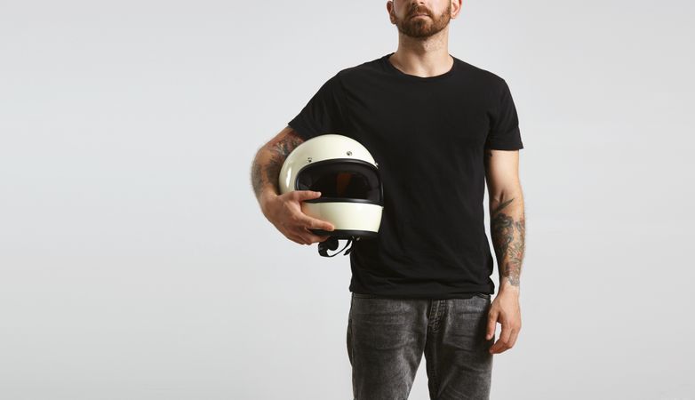 Tattooed man in dark t-shirt holding motorcycle helmet on light background