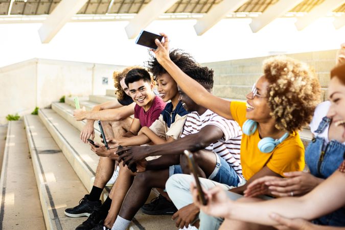 Group of multi-ethnic adults sitting on stairs outside taking picture with phone