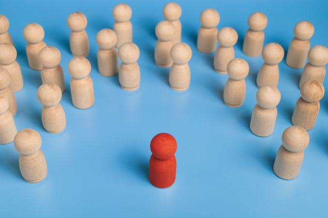 red wooden figure stand to the wooden group crowd. isolated on blue background. leadership and teamwork concept