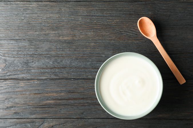 Bowl of sour cream yogurt and spoon on wooden background