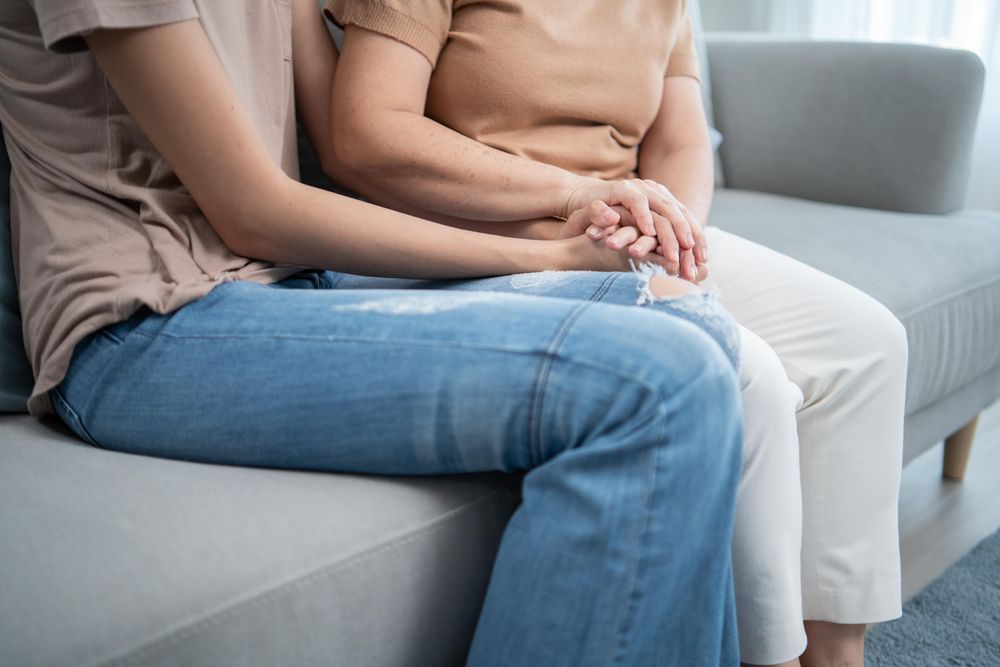 Two women sitting on sofa holding hands