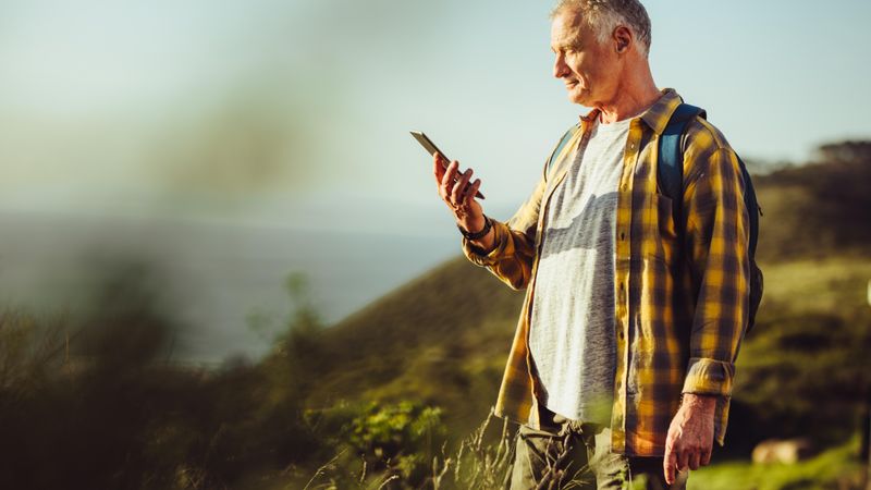 Man looking at his cell phone after a successful trek on a hill