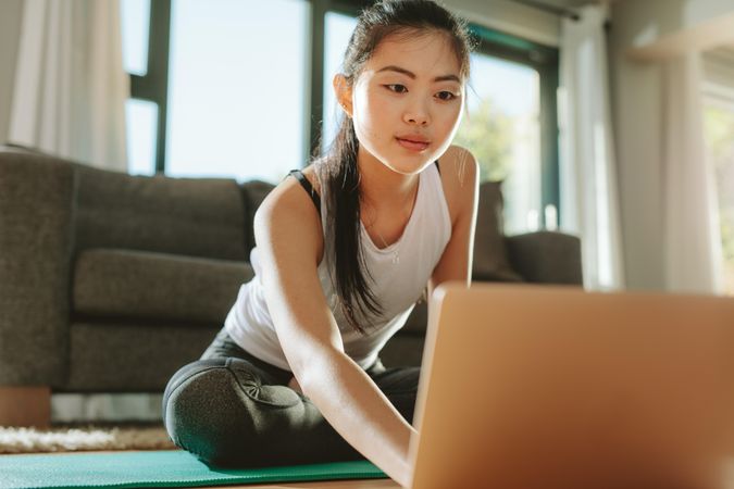 Woman in sportswear sitting on floor and using laptop