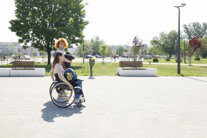 Side view of red haired woman, and woman in a wheelchair walking in park