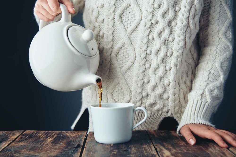 Woman pouring tea from tea pot on wooden table