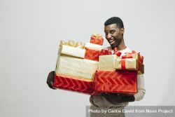 Black man making funny face holding pile of wrapped presents in both arms as glitter falls 43q1V0