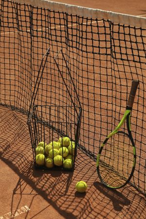 Basket with tennis balls and racket against net on clay court