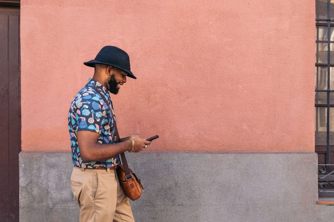 Stylish Black man walking on the city street using smartphone