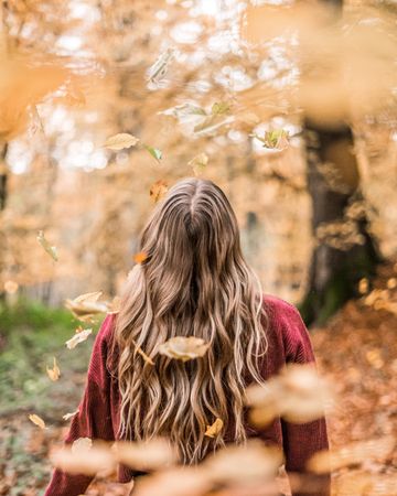 Back view of blonde woman standing in the woods during autumn