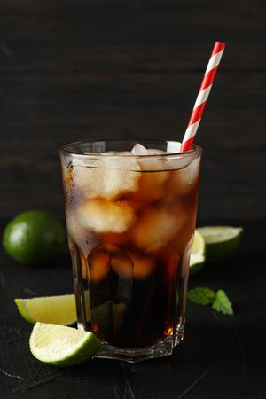 Glass of cold cola and limes on cement background