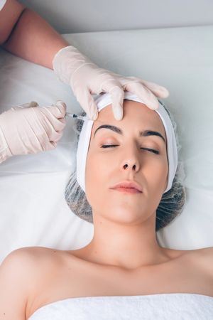 Aesthetician's hands injecting botox into female's forehead in a beauty salon