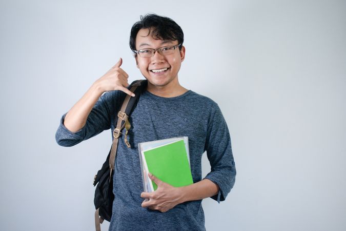 Asian young male student wearing bag and carrying books smiling and happy expression