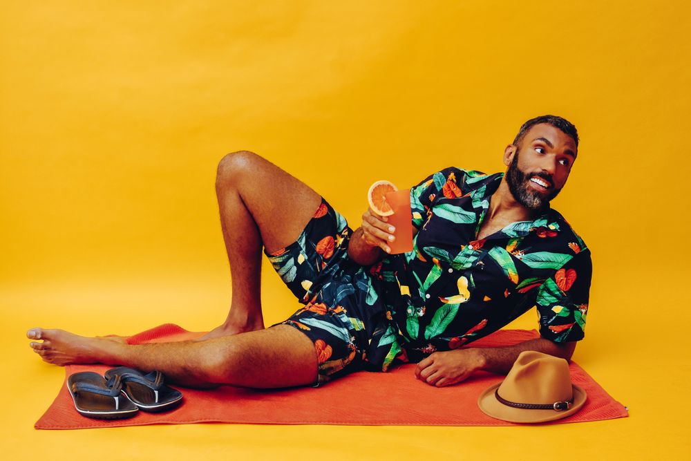 Black male laying back on towel and looking away while holding tropical drink