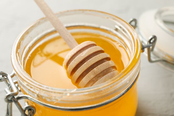 Glass jar with honey and dipper on neutral background, closeup