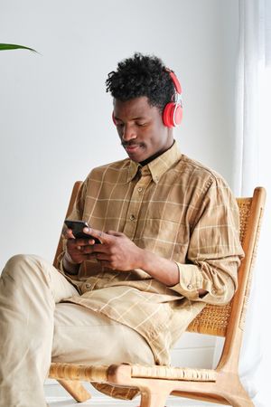 Black man in headset chatting on smartphone on wicker chair