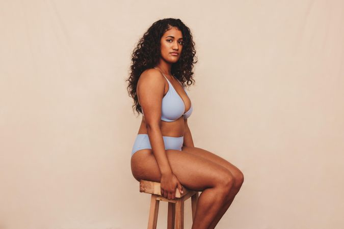 Body positive young woman sitting comfortably in a blue underwear against a studio background