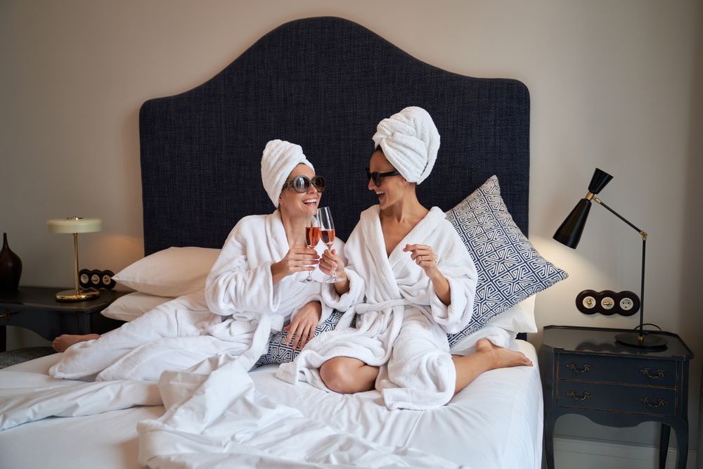 Happy women clinking glasses of champagne resting on bed