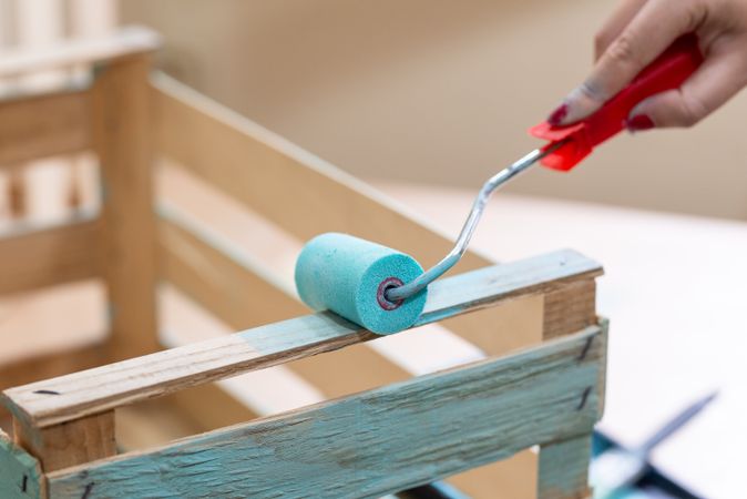 Woman paining wooden box in blue color with roller