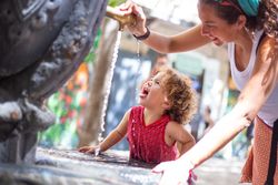 Woman pouring water from fountain for child on street