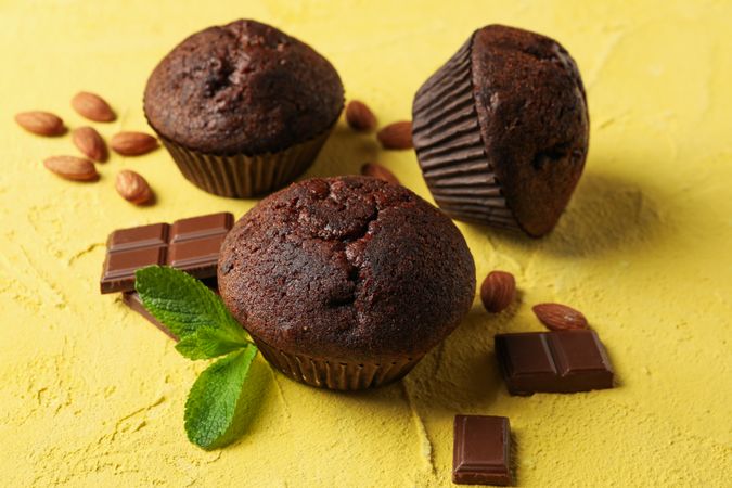 Delicious muffins, chocolate and almond on yellow background