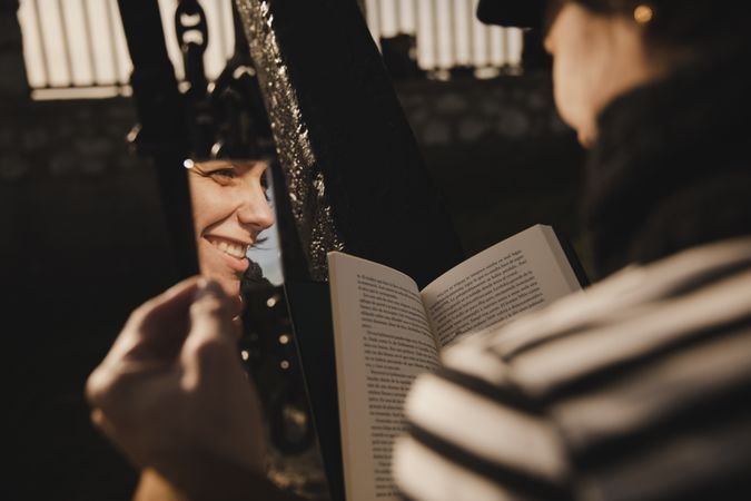 Reflection of smiling woman with book near fence