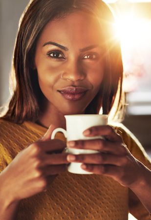 Close up portrait of Black woman with coffee in sunny room