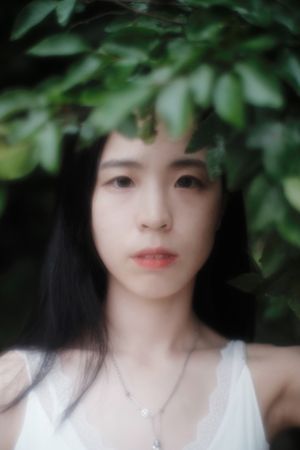 Portrait of neutral young woman in light tank top standing under tree