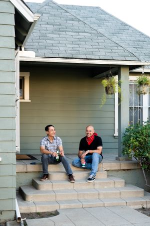 Two men laughing and relaxing with a beer on front porch after work
