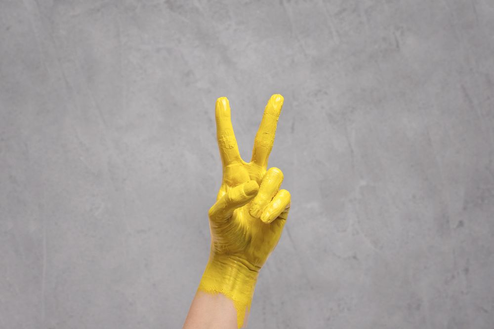 Hand painted yellow giving the peace sign on gray background for Pantone color of 2021