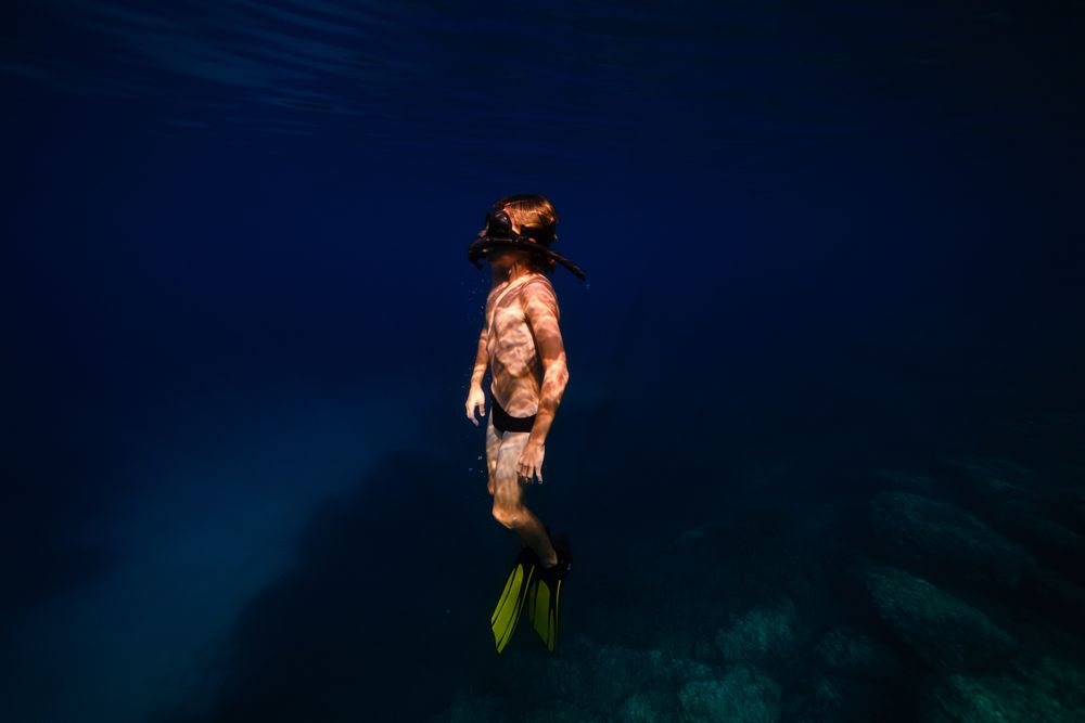Teen boy in flippers swimming undersea in daylight