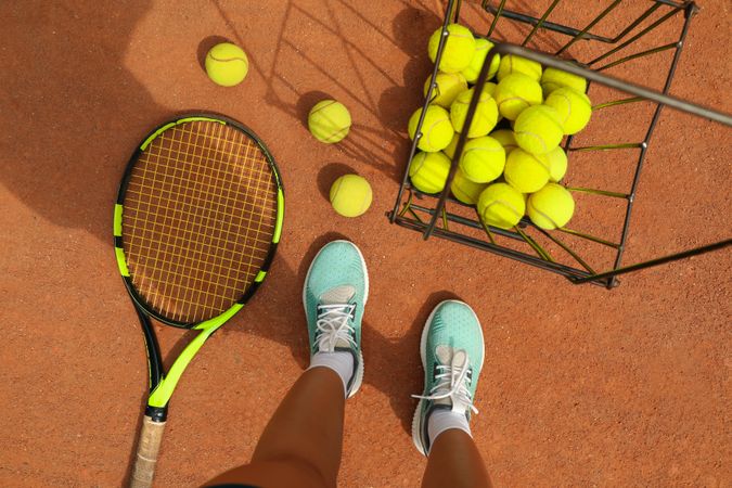 Woman feets, racket and tennis balls on clay court